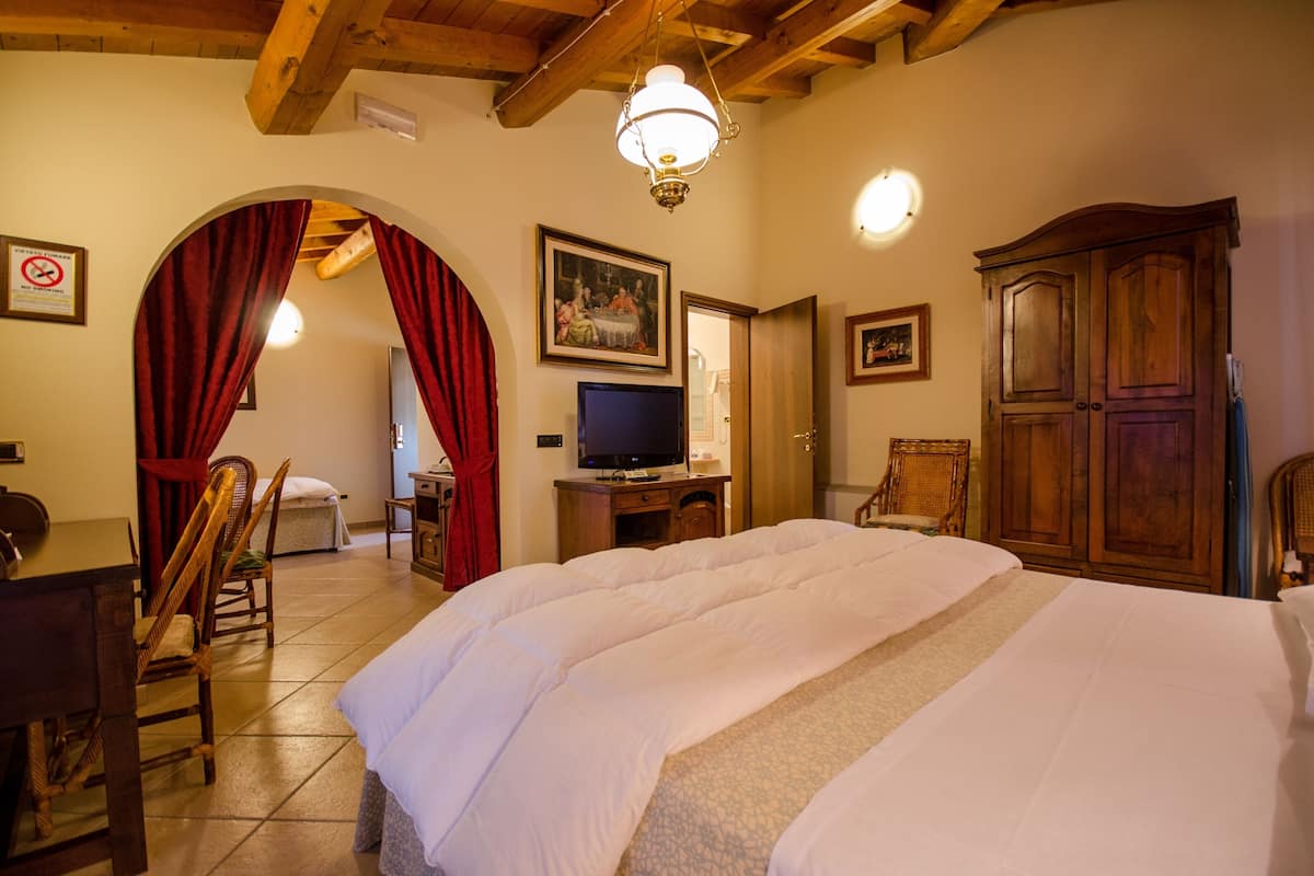A hotel room with a large bed, wooden furniture, a television, and a chandelier.