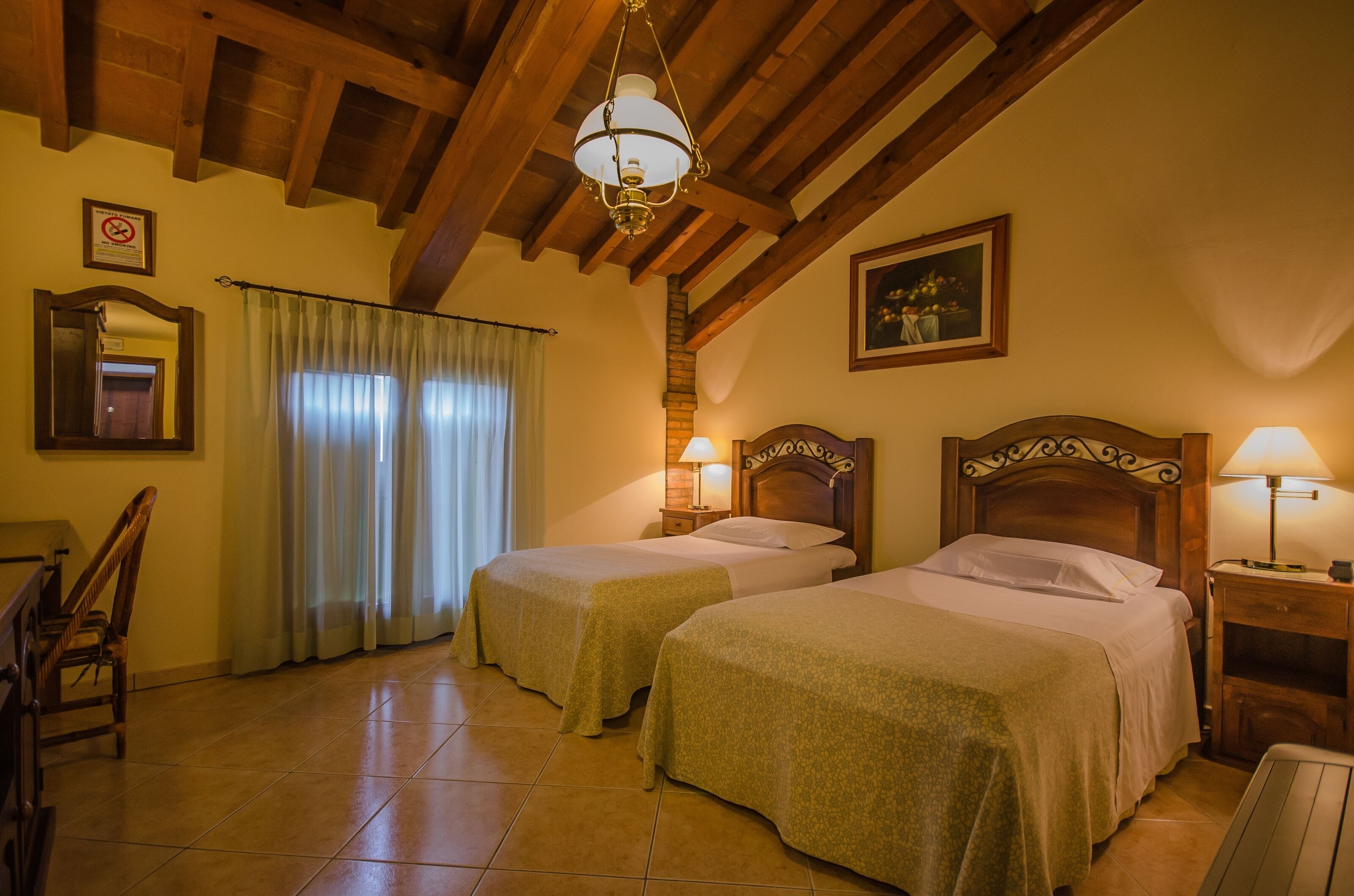 A room with two beds, wooden beams on the ceiling, a chandelier, a painting, and a mirror on the wall.