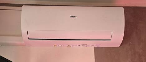 Un aire acondicionado Haier blanco montado en una pared, con un televisor de pantalla plana debajo.