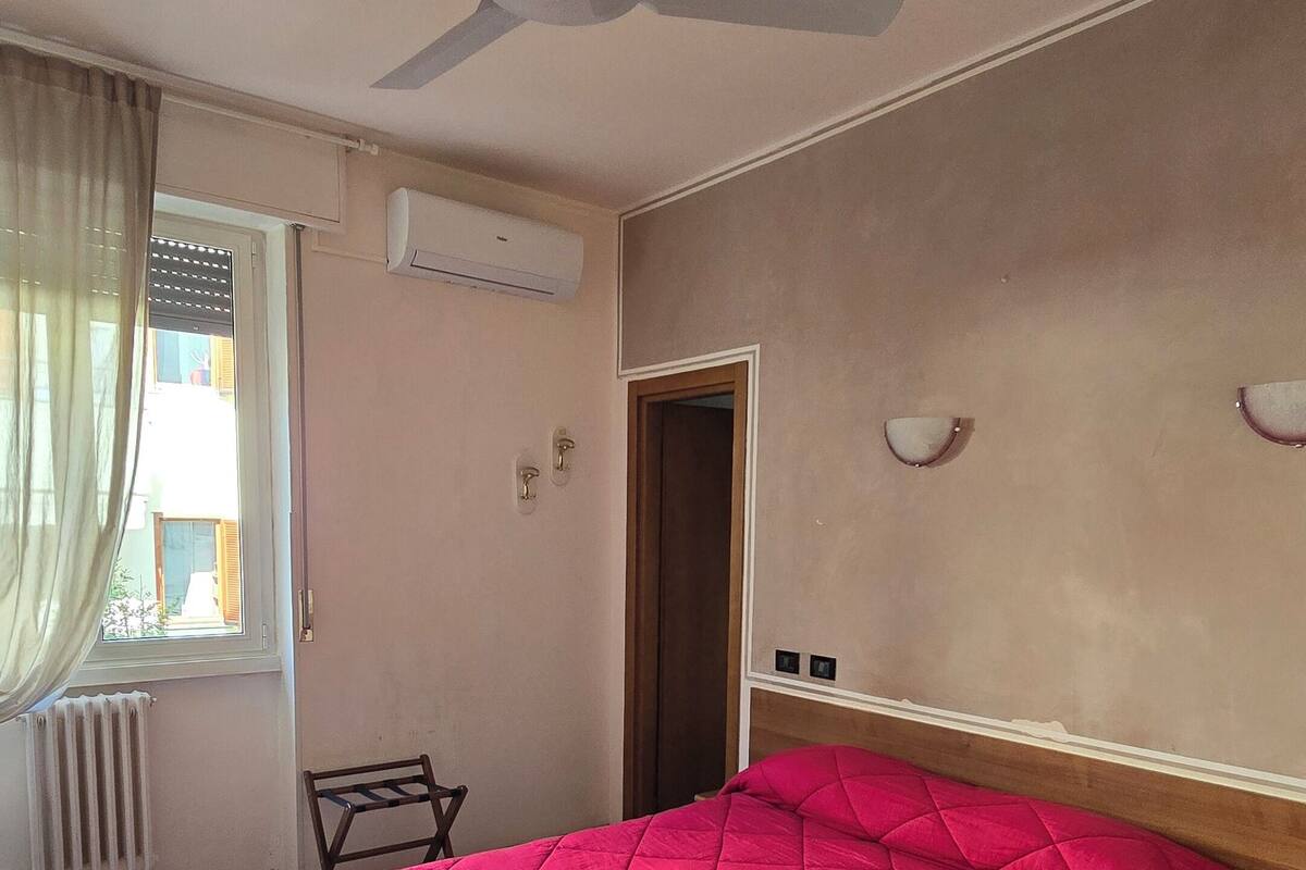 A bedroom with a bed, a ceiling fan, a window with curtains, and an air conditioning unit.