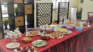 Une table de buffet garnie de divers plats et boissons, entourée d’étagères où sont exposés des objets décoratifs, avec une fenêtre en arrière-plan.