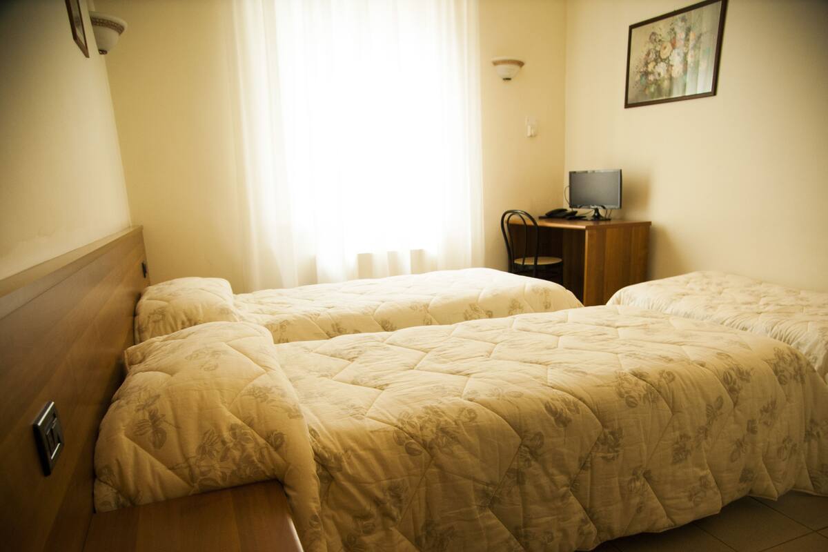 A hotel room with two beds, a desk, a chair, and a television.