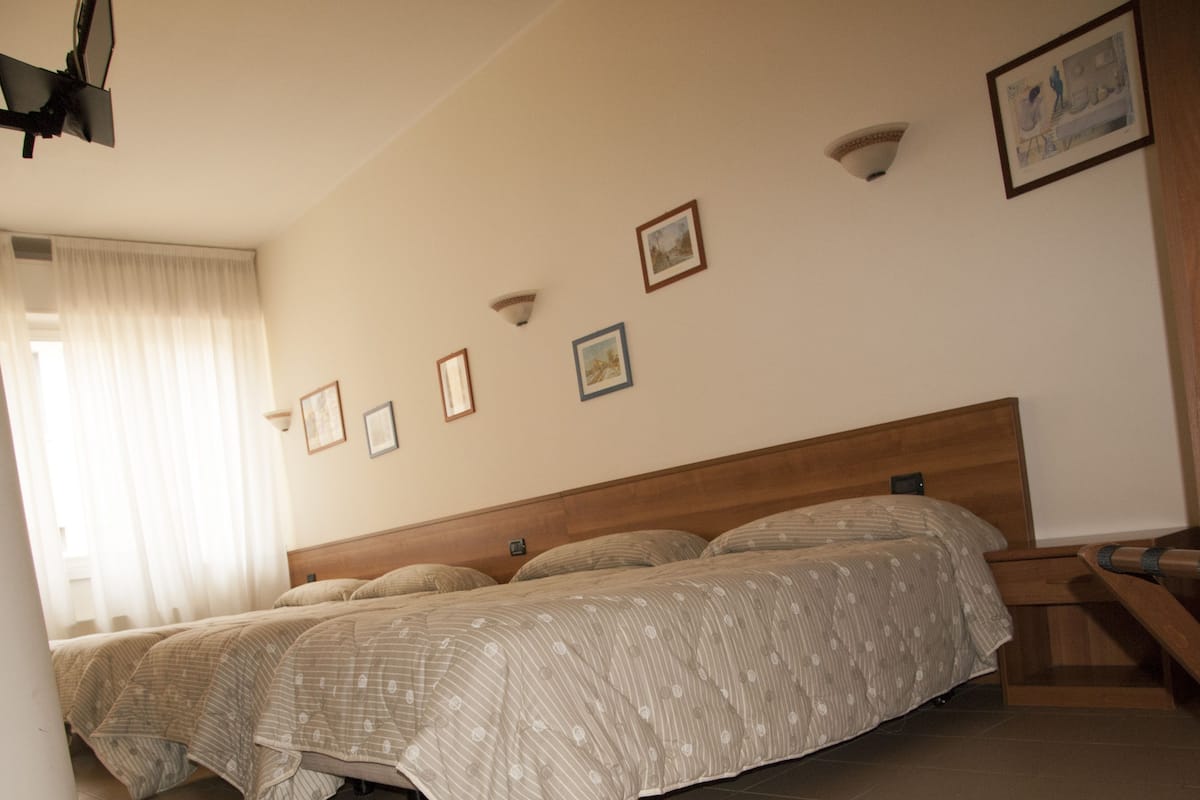 A bedroom with two beds, a wooden headboard, a window with curtains, and several framed pictures on the wall.