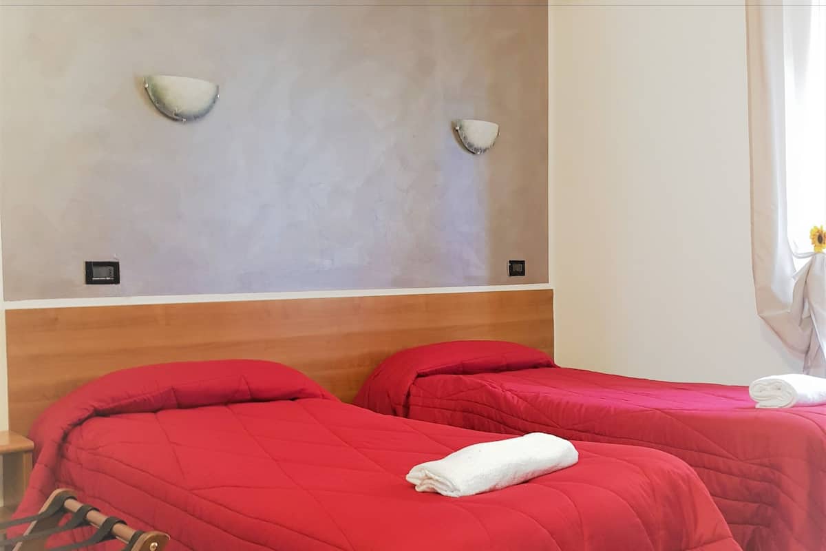 A hotel room with two beds, a wooden chair, a ceiling fan, and a wall-mounted light fixture.