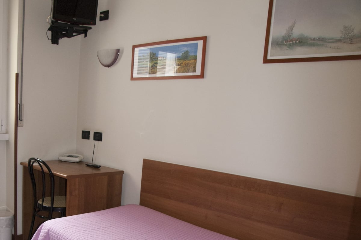 A bedroom with a bed, a desk, a chair, and a television mounted on the wall.