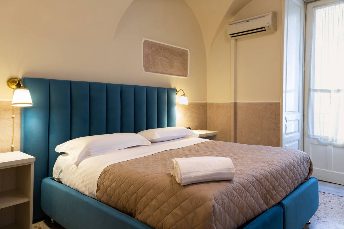 A bedroom with a bed, nightstands, a wall-mounted air conditioner, and a window.