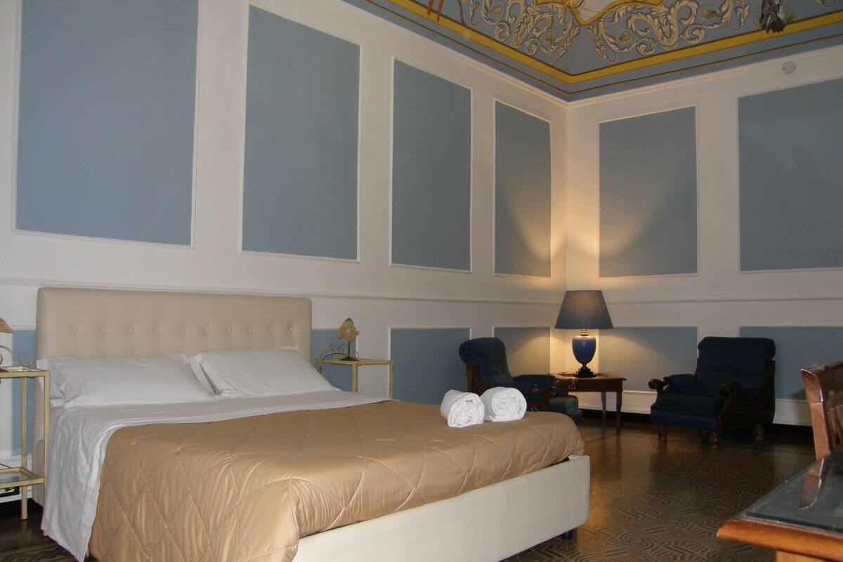 A hotel room with a large bed, two chairs, a table, and a lamp.
