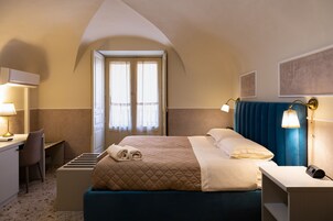 Quarto de hotel com cama, abajures, escrivaninha e uma cadeira.
