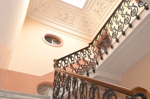 Uma escadaria com grades de metal ricamente decoradas e teto ornamental.