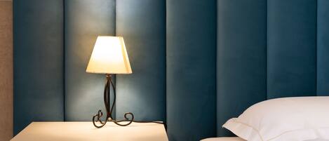 A neatly made bed with a white pillow and a bedside table with a lamp.