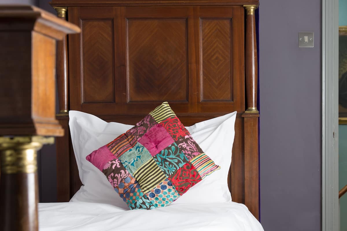A bed with a white pillow and a colorful patchwork quilt.