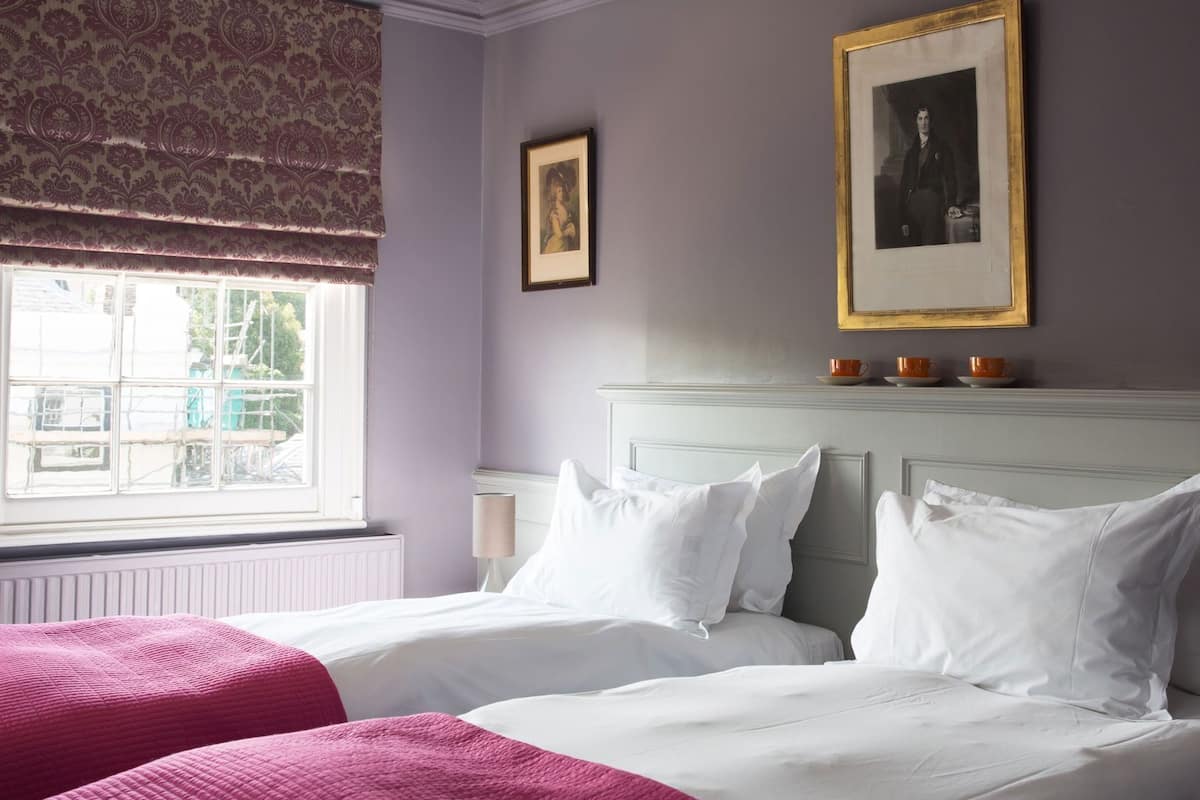 A bedroom with two beds, a window with a view, and a framed picture on the wall.
