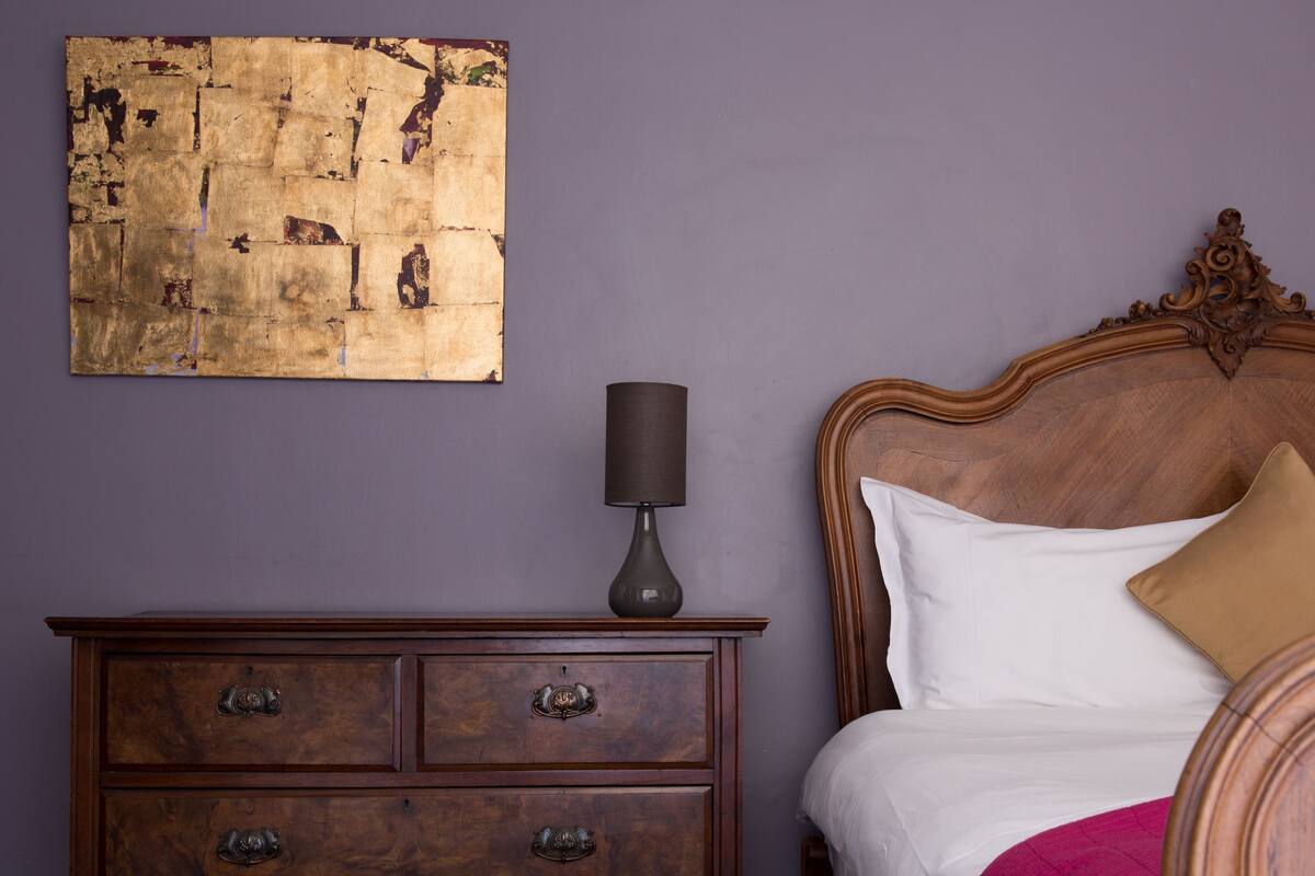 A bedroom with a wooden bed, a nightstand, a lamp, and a large abstract painting on the wall.