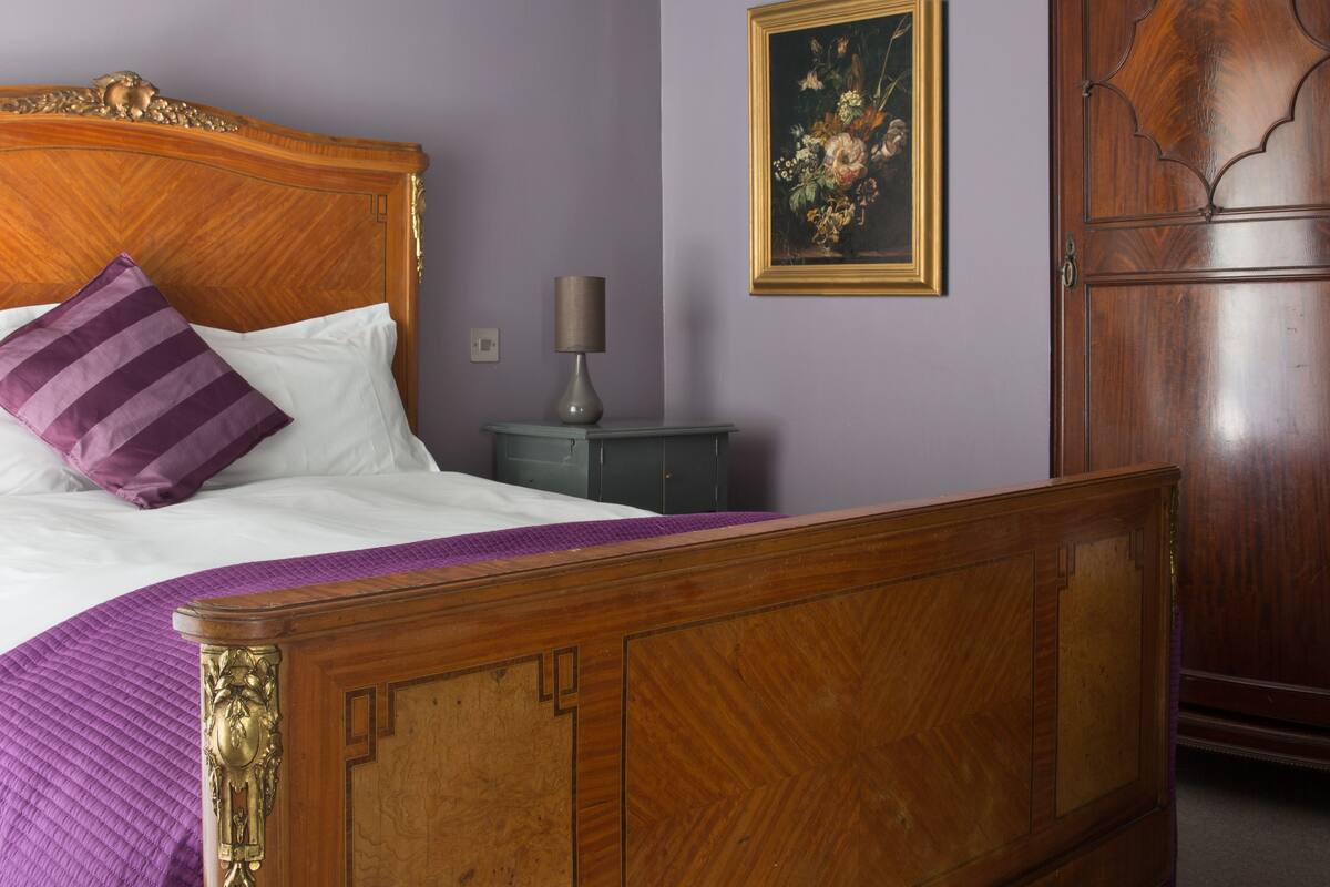 A wooden bed with a headboard, a purple pillow, and a green nightstand with a lamp.