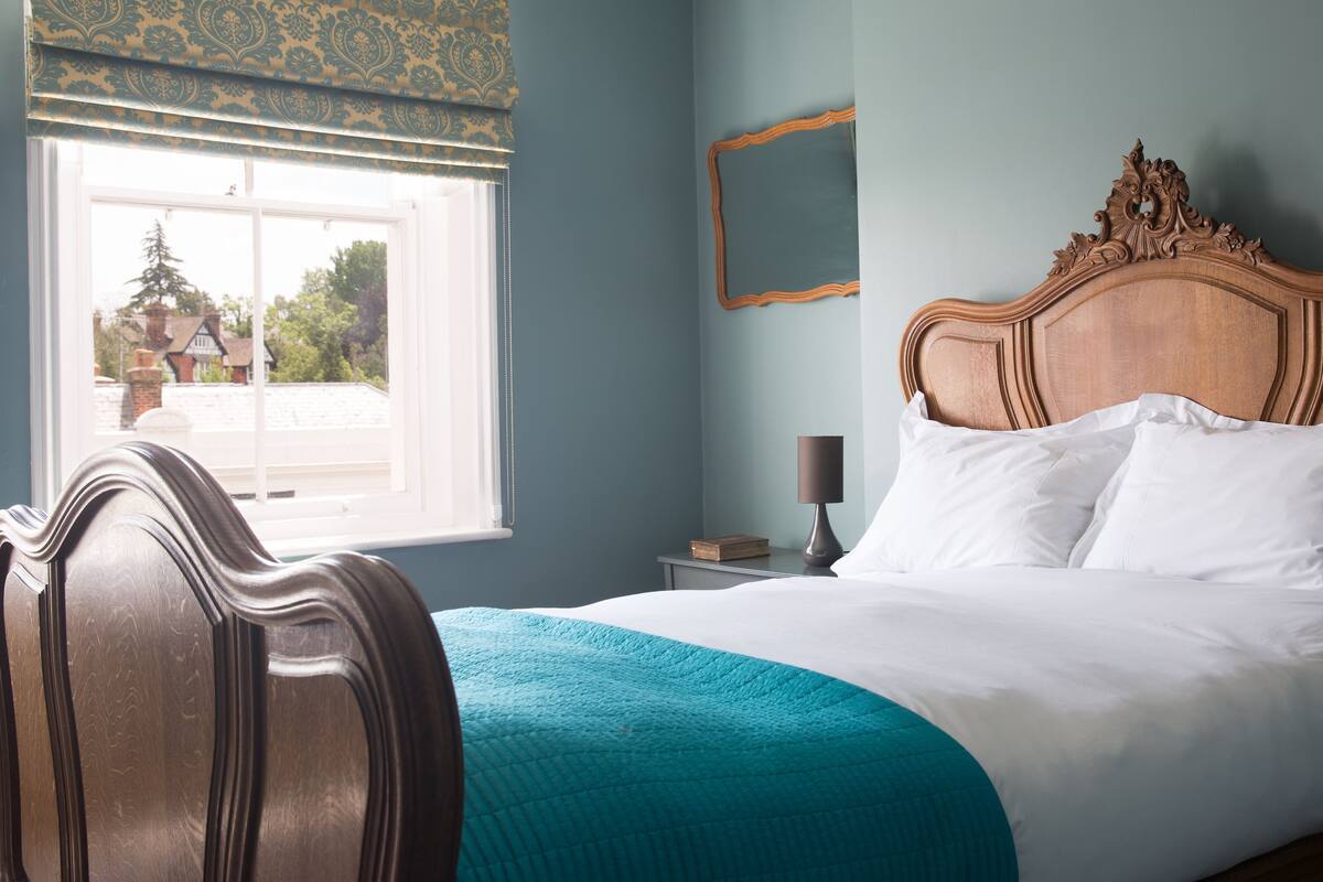 A neatly made bed with white linens and a teal throw blanket, a wooden headboard, and a bedside table with a lamp.