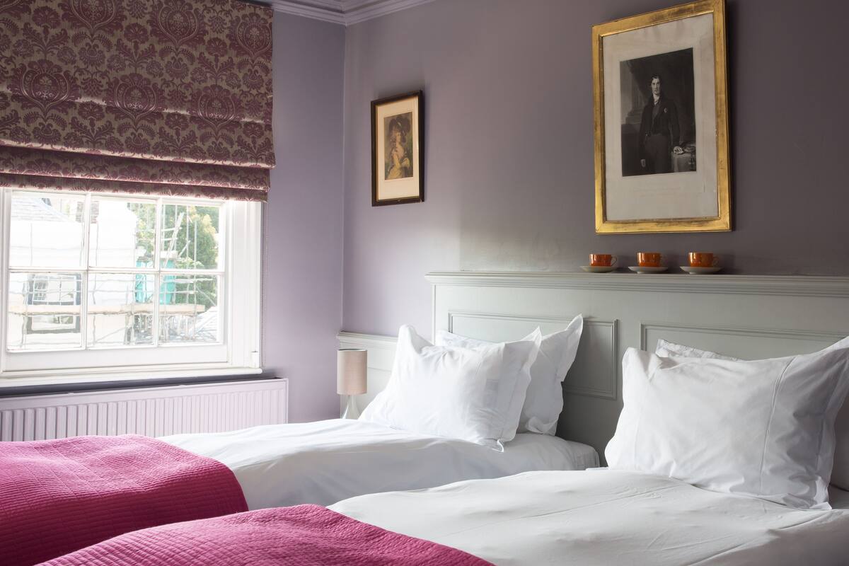 A bedroom with two beds, a window with a view, and a framed picture on the wall.