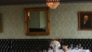 Uma sala de jantar formal com uma mesa comprida posta para uma refeição, um candelabro e um espelho na parede.