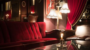 Um sofá de veludo vermelho, uma mesa de vidro com uma vela e uma luminária em um ambiente acolhedor.