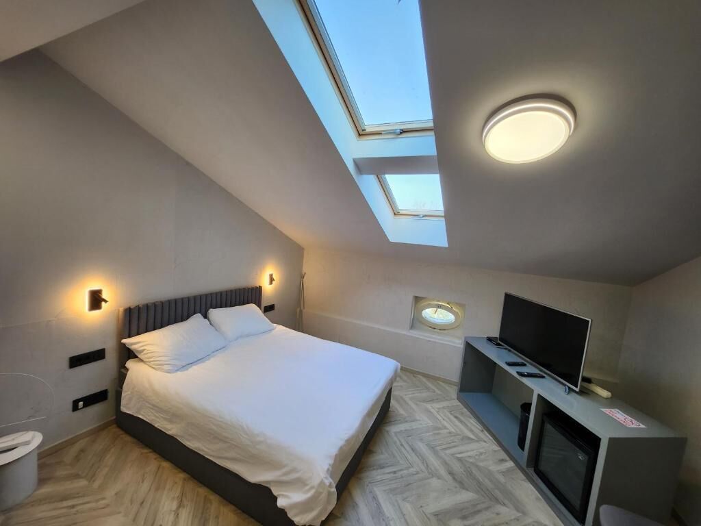 A bedroom with a bed, skylight, TV, and a small window.