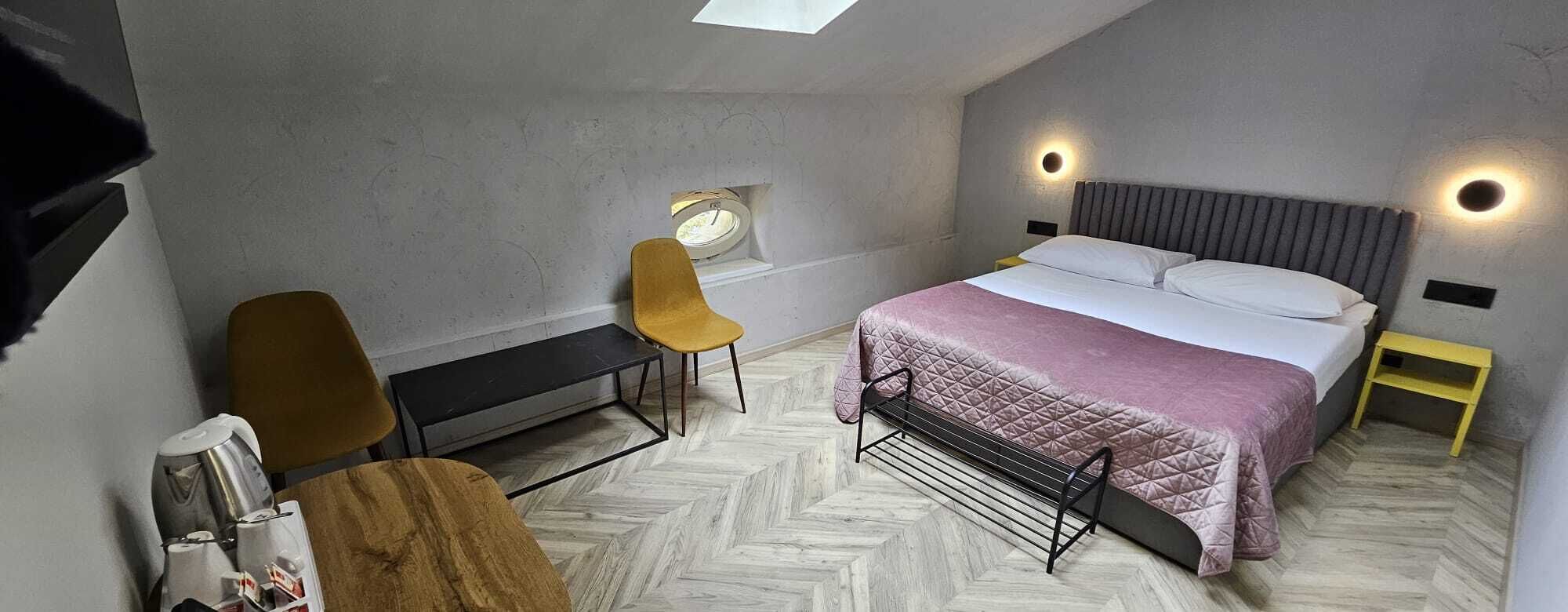 A compact bedroom with a bed, two chairs, a bench, a small table, and a window.