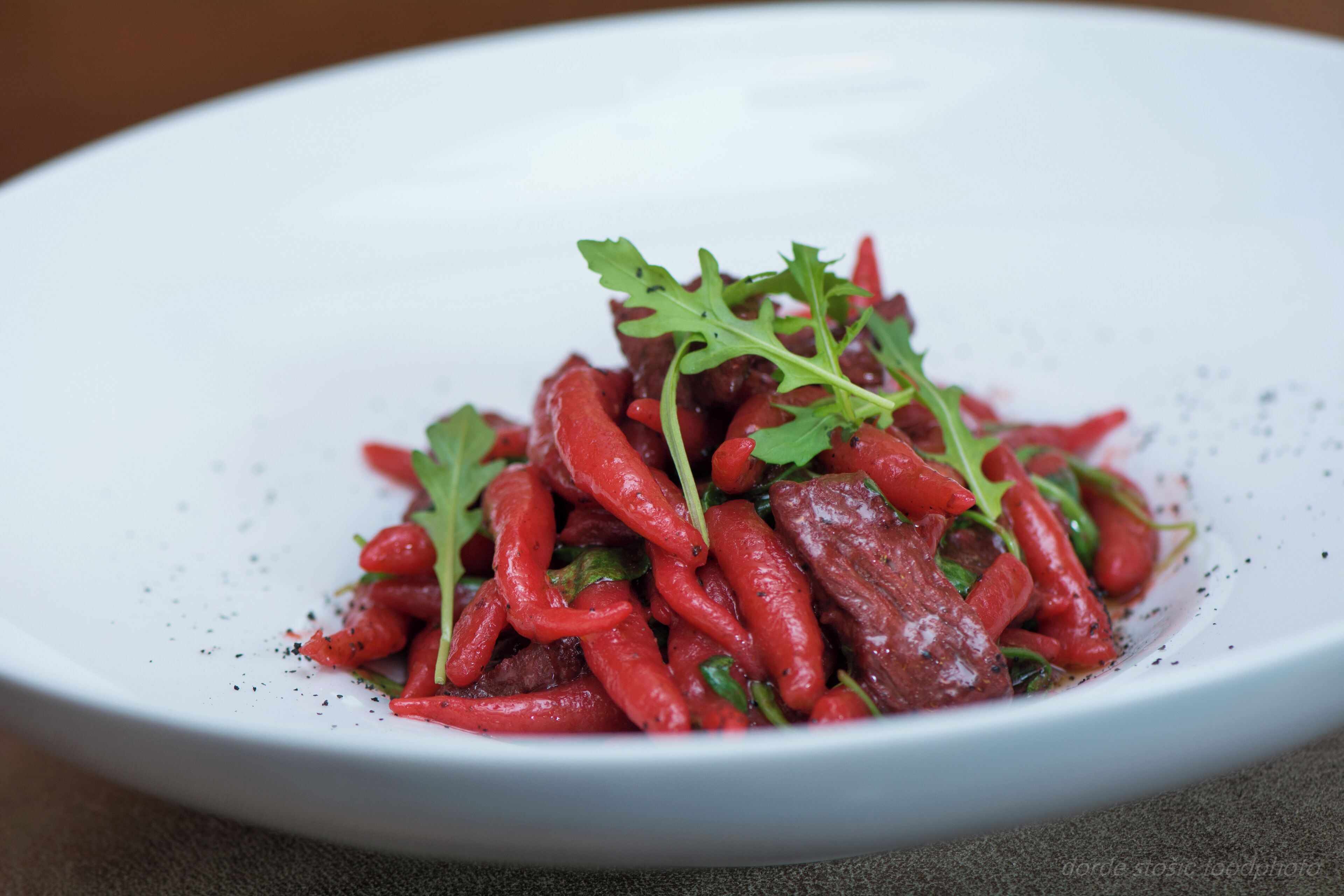 Un plato blanco con una porción de chiles rojos y vegetales verdes.