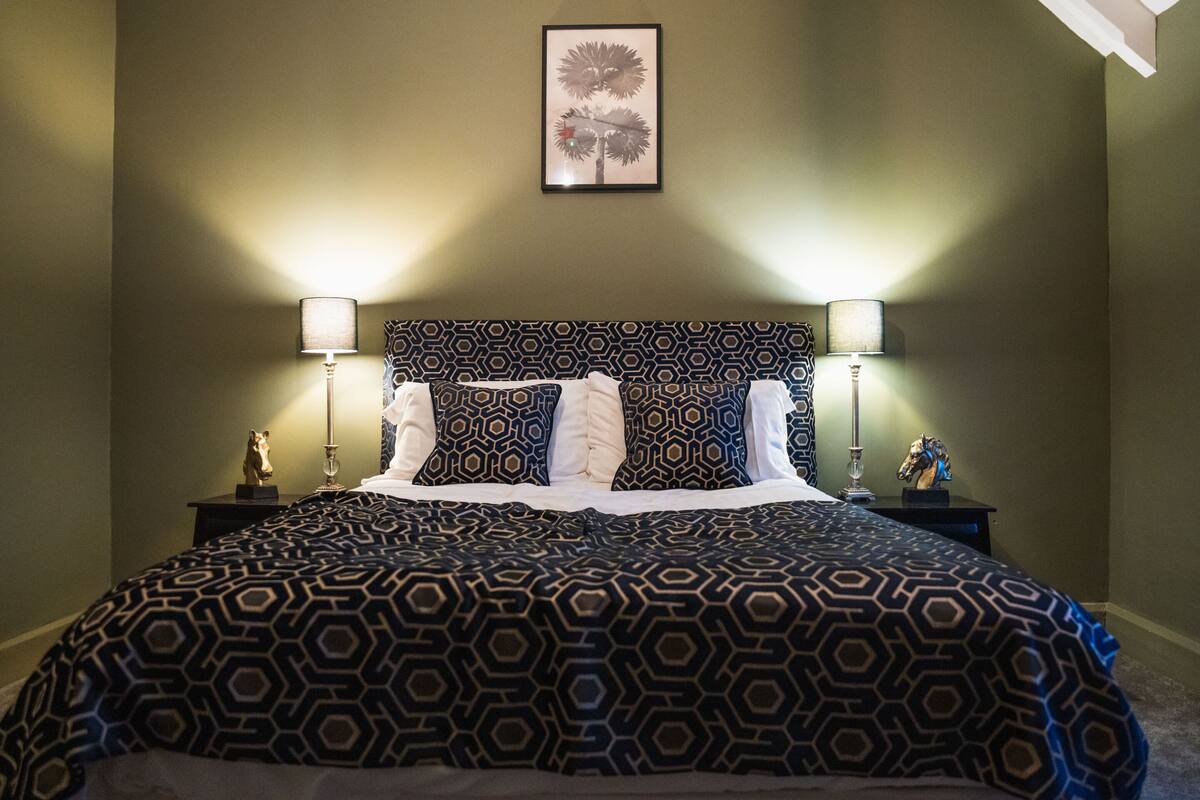 A neatly made bed with a geometric patterned bedspread, two bedside lamps, and a framed picture on the wall.