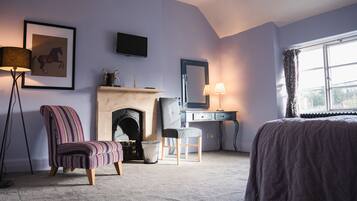 A bedroom with a bed, a chair, a desk, a fireplace, a television, and a window with curtains.