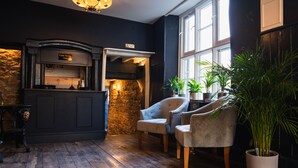 Une pièce chaleureuse avec une cheminée en pierre, deux fauteuils confortables, un plancher en bois et une vue sur l’extérieur grâce à de grandes fenêtres.
