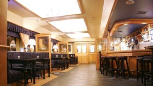 Una zona de bar con taburetes de madera, una barra y un área de estar con sillas y mesas estampadas.