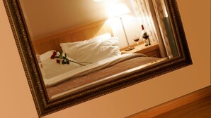 Una habitación de hotel con una cama, una mesita de noche con lámpara y un espejo que refleja el cuarto.