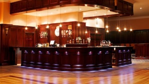Una zona de bar con una barra de madera curva, luces colgantes y un reloj en la pared.