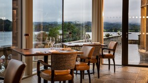 A restaurant with tables and chairs, large windows, and a view of a body of water and greenery. - Langdale Chase Hotel (Windermere)