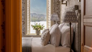 A bedroom with a bed, two lamps, a window with a view of a lake, and a vase with flowers. - Langdale Chase Hotel (Windermere)