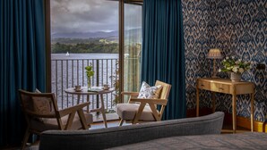 A room with a view of a lake and mountains, a wooden chair, a small table with a cup and saucer, and a lamp on a wooden side table. - Langdale Chase Hotel (Windermere)
