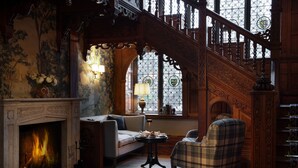 A traditional interior with a fireplace, a sofa, a plaid armchair, and a staircase with stained glass windows. - Langdale Chase Hotel (Windermere)
