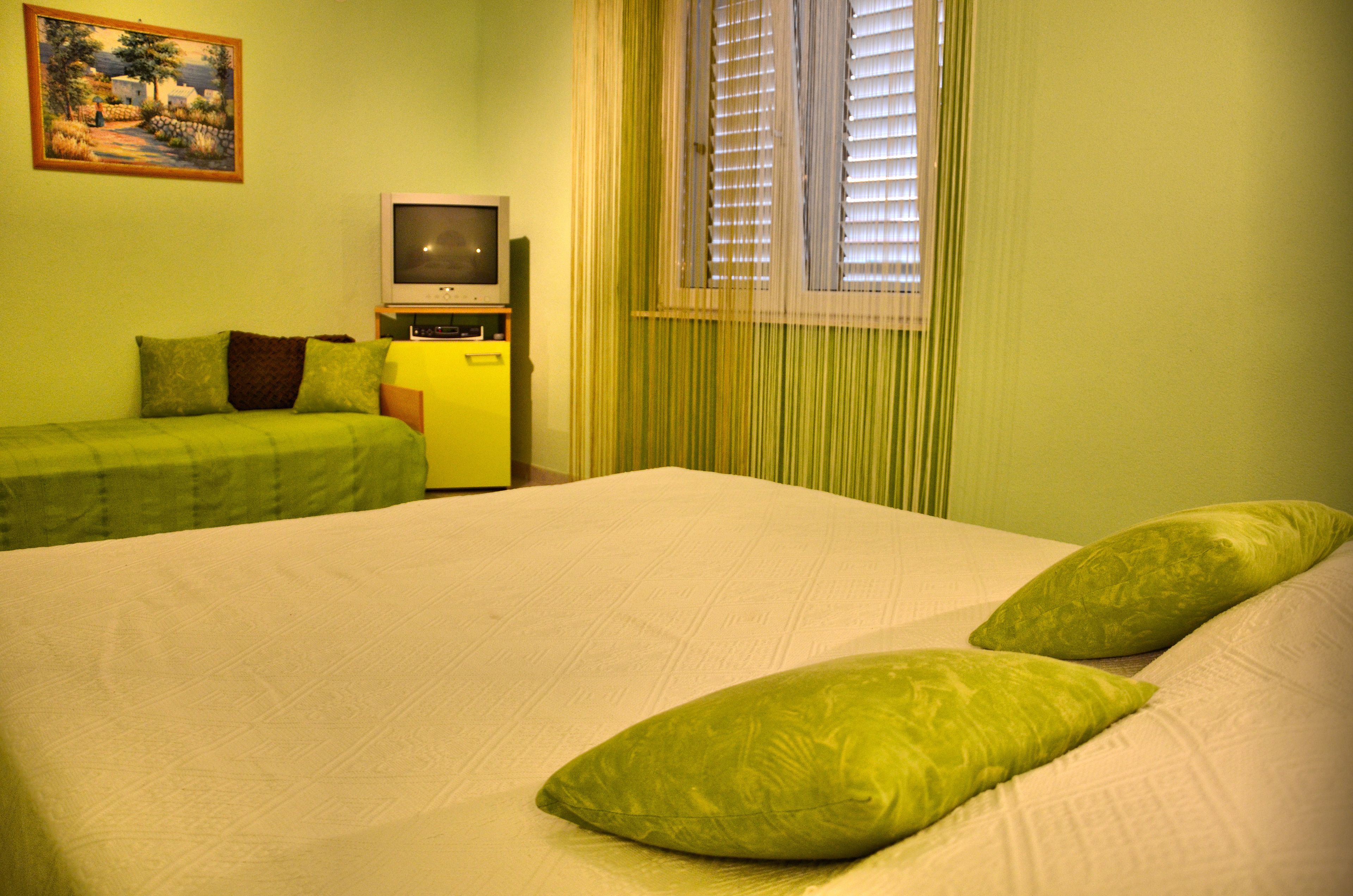 A room with a bed, two green pillows, a TV, and a painting on the wall.
