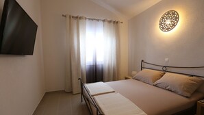 A bedroom with a bed, curtains, a wall-mounted TV, and a decorative light fixture. - Villa Mediteran (Okrug)