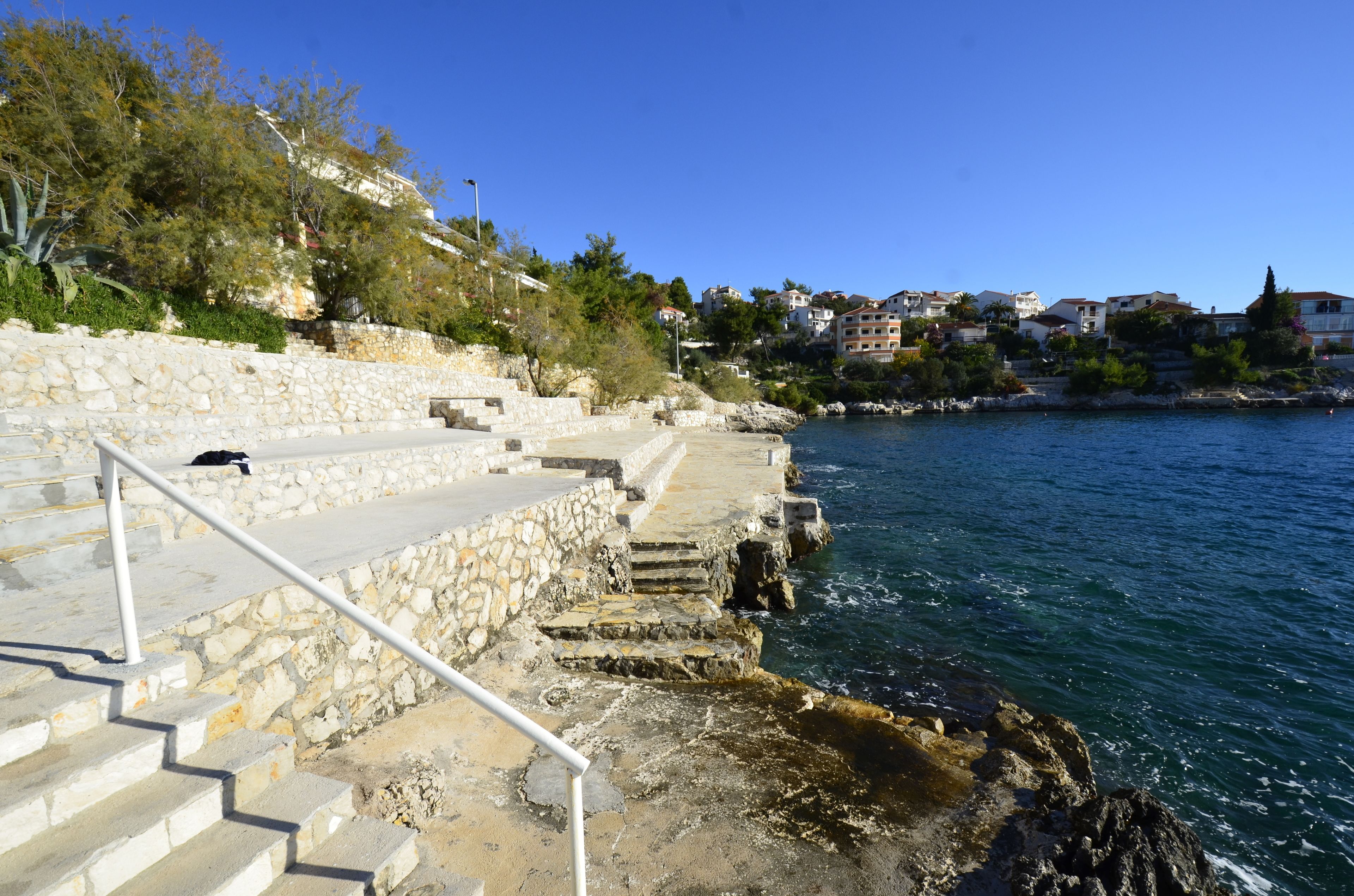 A coastal staircase leading to a stone platform by the sea, with buildings in the background.