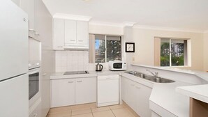 Uma cozinha moderna com armários brancos, micro-ondas, chaleira e máquina de lavar louça.