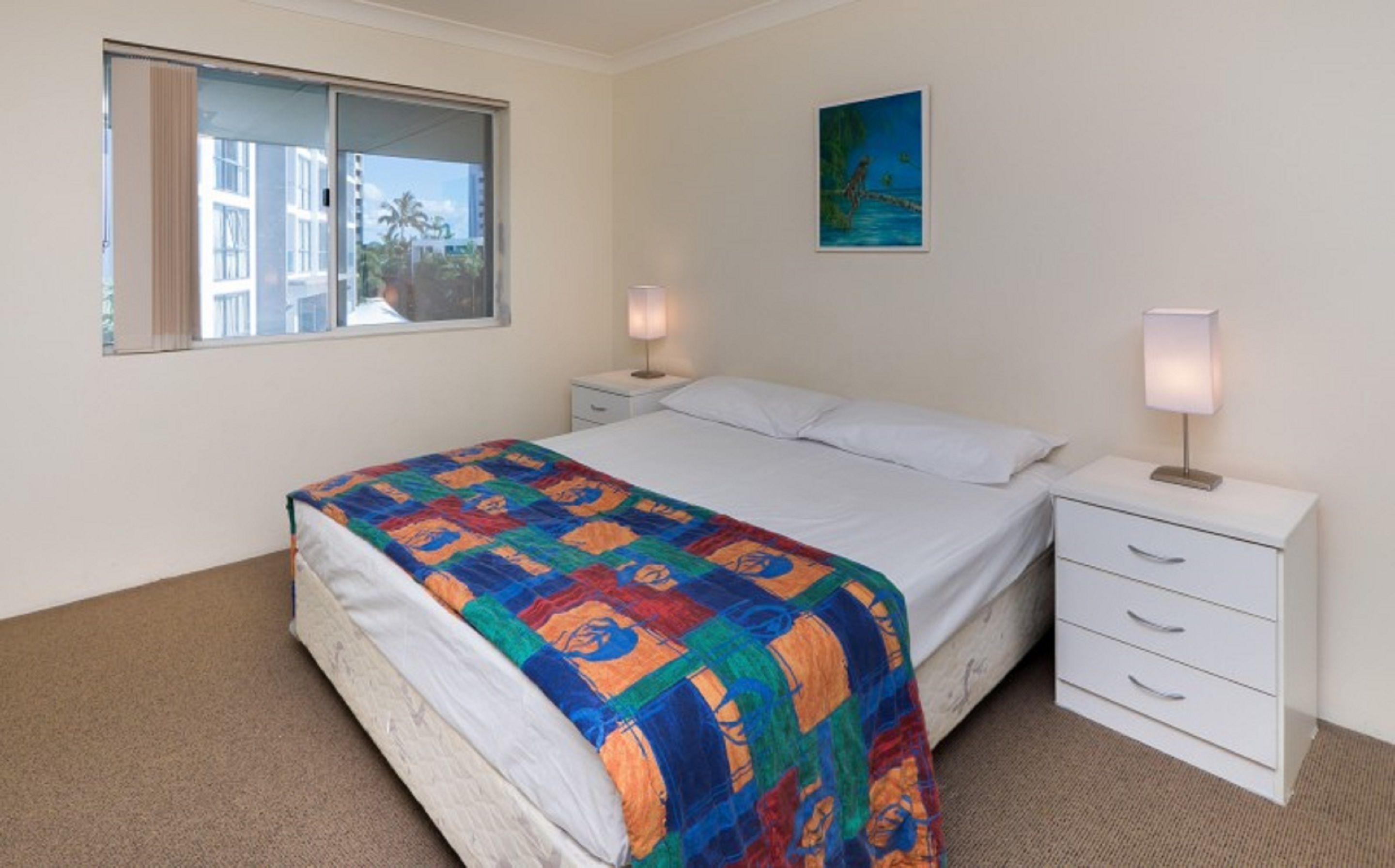 A bedroom with a bed, two bedside tables with lamps, a window, and a painting on the wall.
