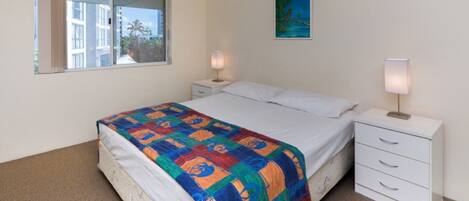 A bedroom with a bed, two bedside tables with lamps, a window, and a painting on the wall.