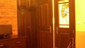 A room with wooden cabinets, a television on a stand, and a door with a glass panel. - Mythos Guesthouse (Kalabaka)