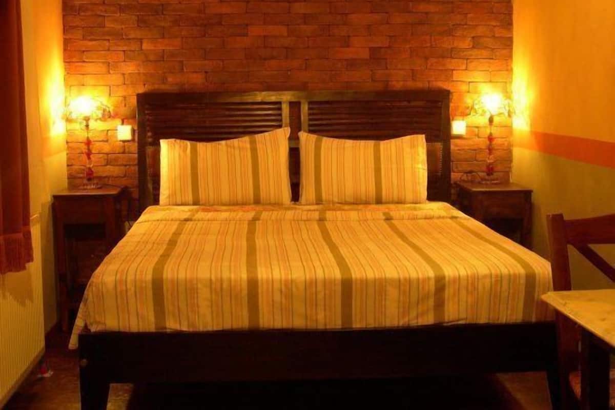A bed with a striped bedspread and two pillows, flanked by nightstands with lamps, against a brick wall.