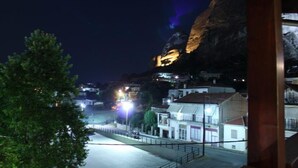 A nighttime view of a coastal town with buildings illuminated against a cliff backdrop. - Mythos Guesthouse (Kalabaka)