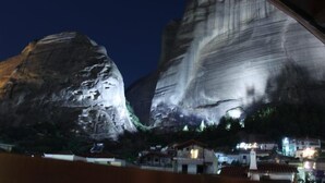 A large rock formation with a small building at its base. - Mythos Guesthouse (Kalabaka)