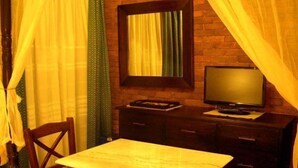 A room with a wooden table, a television on a wooden stand, a mirror, and curtains. - Mythos Guesthouse (Kalabaka)