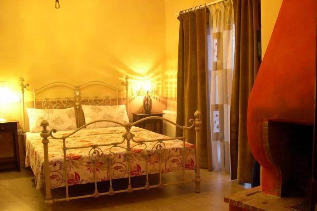 A bedroom with a bed, a nightstand, a lamp, and a fireplace.