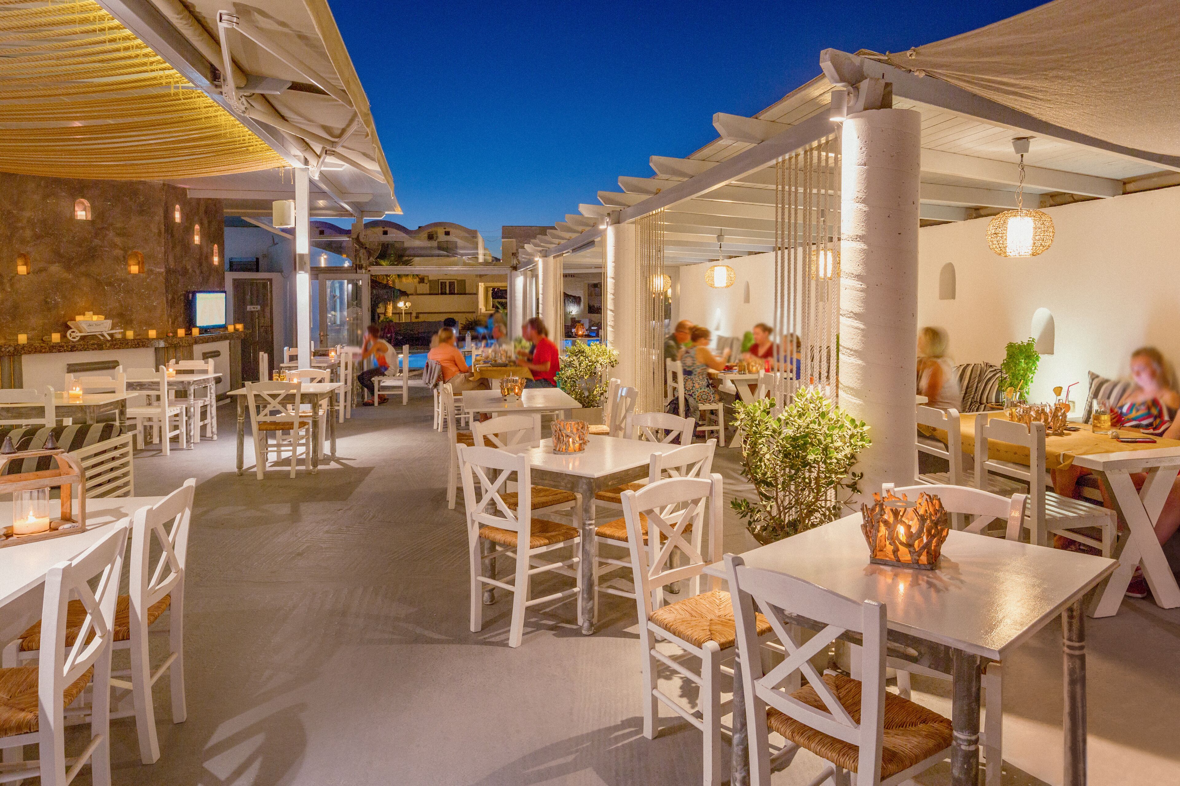 An outdoor dining area with white tables and chairs, surrounded by a covered patio.