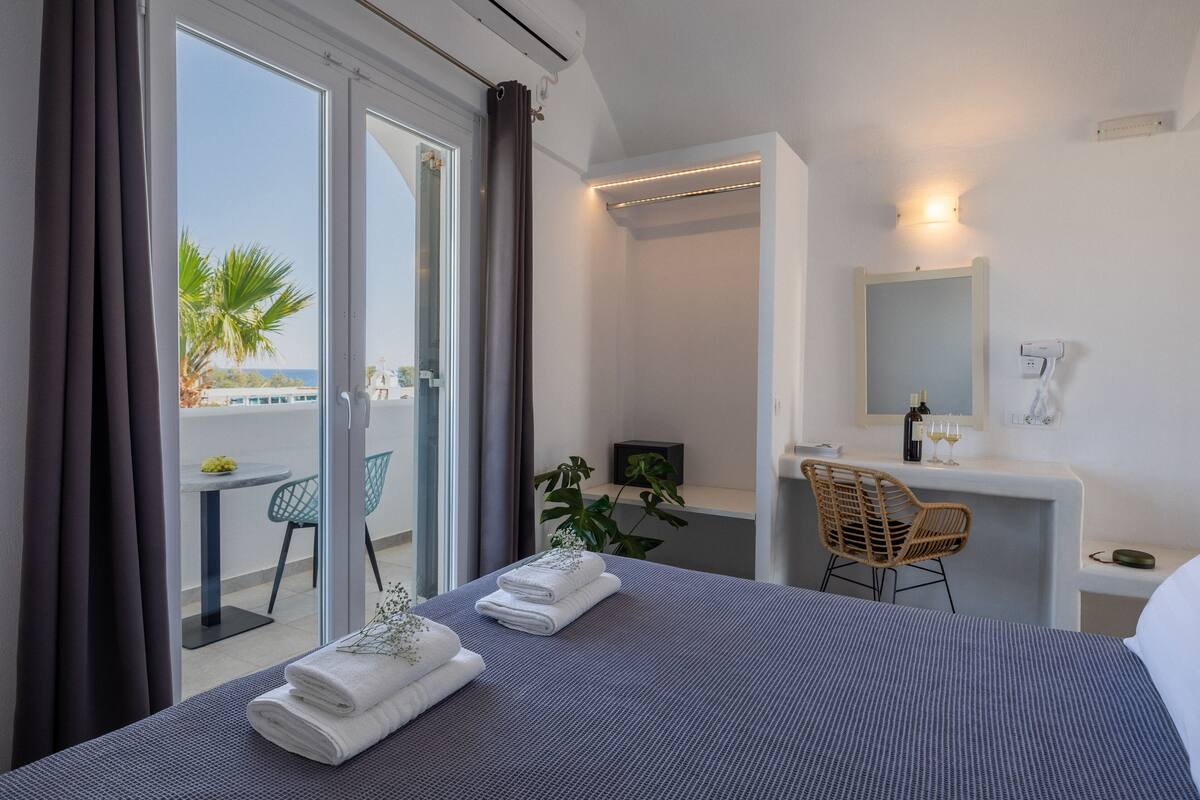 Quarto de hotel com cama, escrivaninha, cadeira, banheiro e varanda com vista.