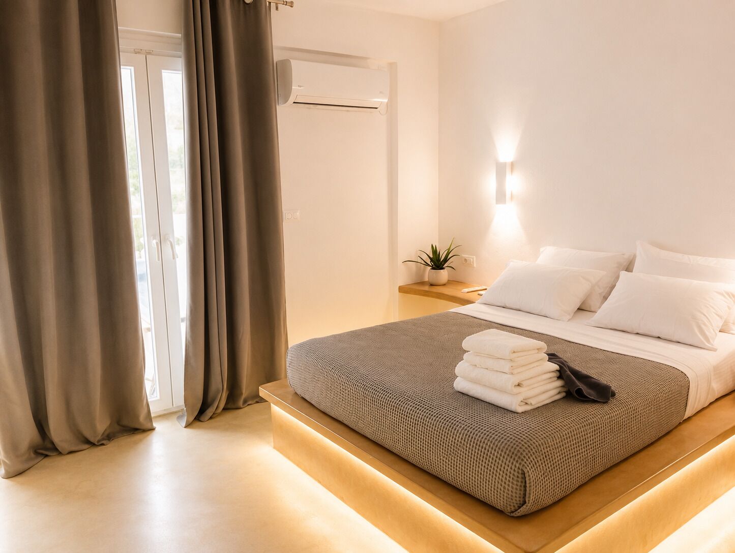Habitación de hotel con cama, cortinas, mesita de noche con una planta y aire acondicionado de pared.